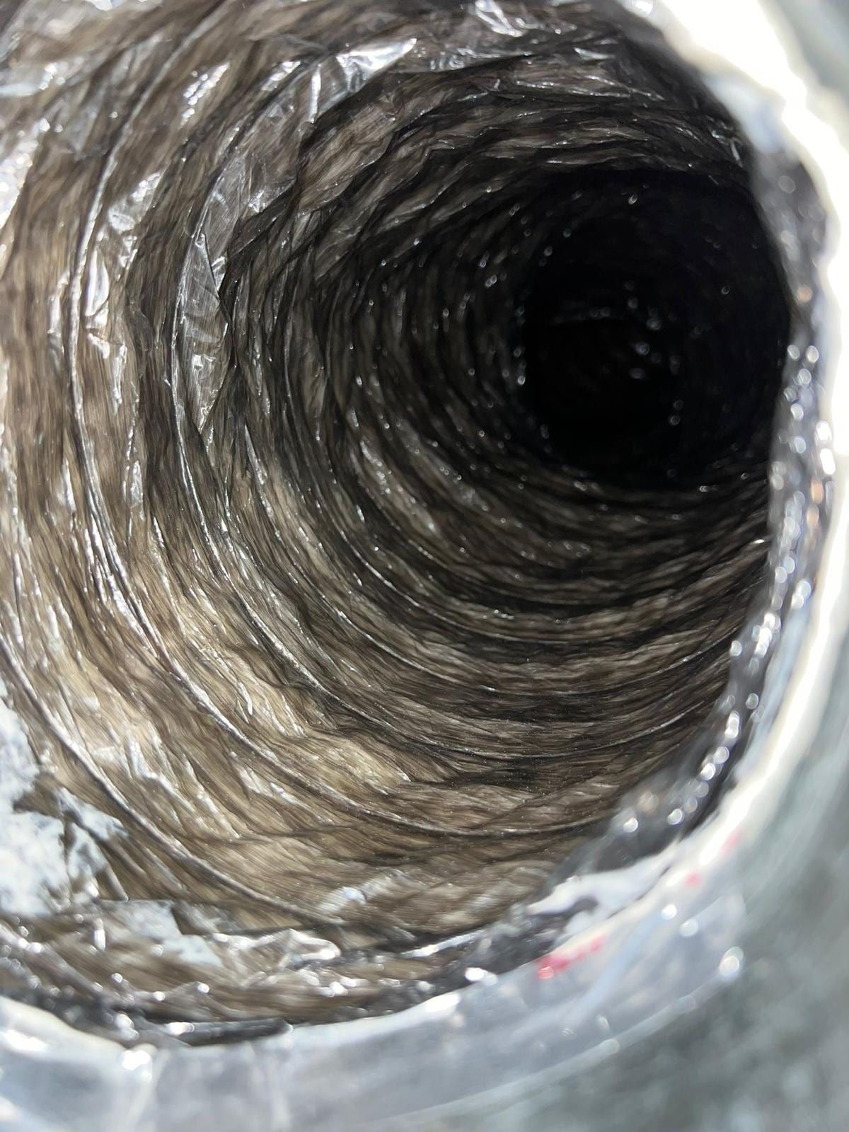 Interior de un ducto de aire antes de la limpieza, con una gruesa capa de polvo gris compactada en las paredes de metal en espiral