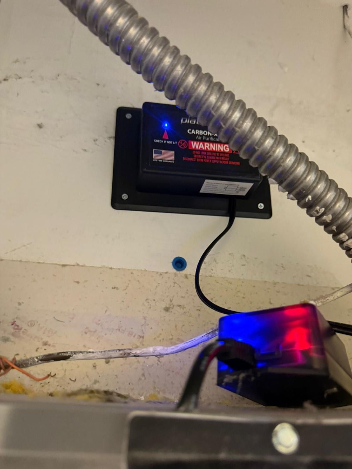 Un purificador de aire UV instalado en los ductos de un clóset de servicio, con su luz indicadora encendida